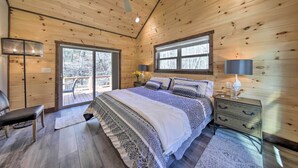 Ein Schlafzimmer einer Holzhütte mit einem Bett, Nachttischen, einem Schreibtisch und einem Sessel.