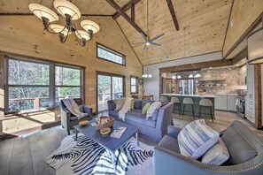 A spacious living room with a large sofa, a coffee table, and a zebra-patterned rug. There are large windows allowing natural light and views of the outdoors. - Airy Ellijay Home w/ Spacious Creekside Deck! (Ellijay)