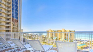 A balcony with white lounge chairs and a small table, overlooking a beach and hotel buildings. - Lagoon-View Balcony! Family Resort Escape in PCB (Panama City Beach)