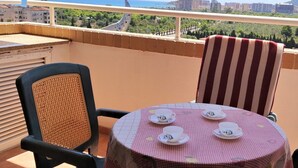 Ein Balkon mit Tisch, der für Tee gedeckt ist, ein gestreifter Stuhl und Blick auf das Meer und Gebäude.
