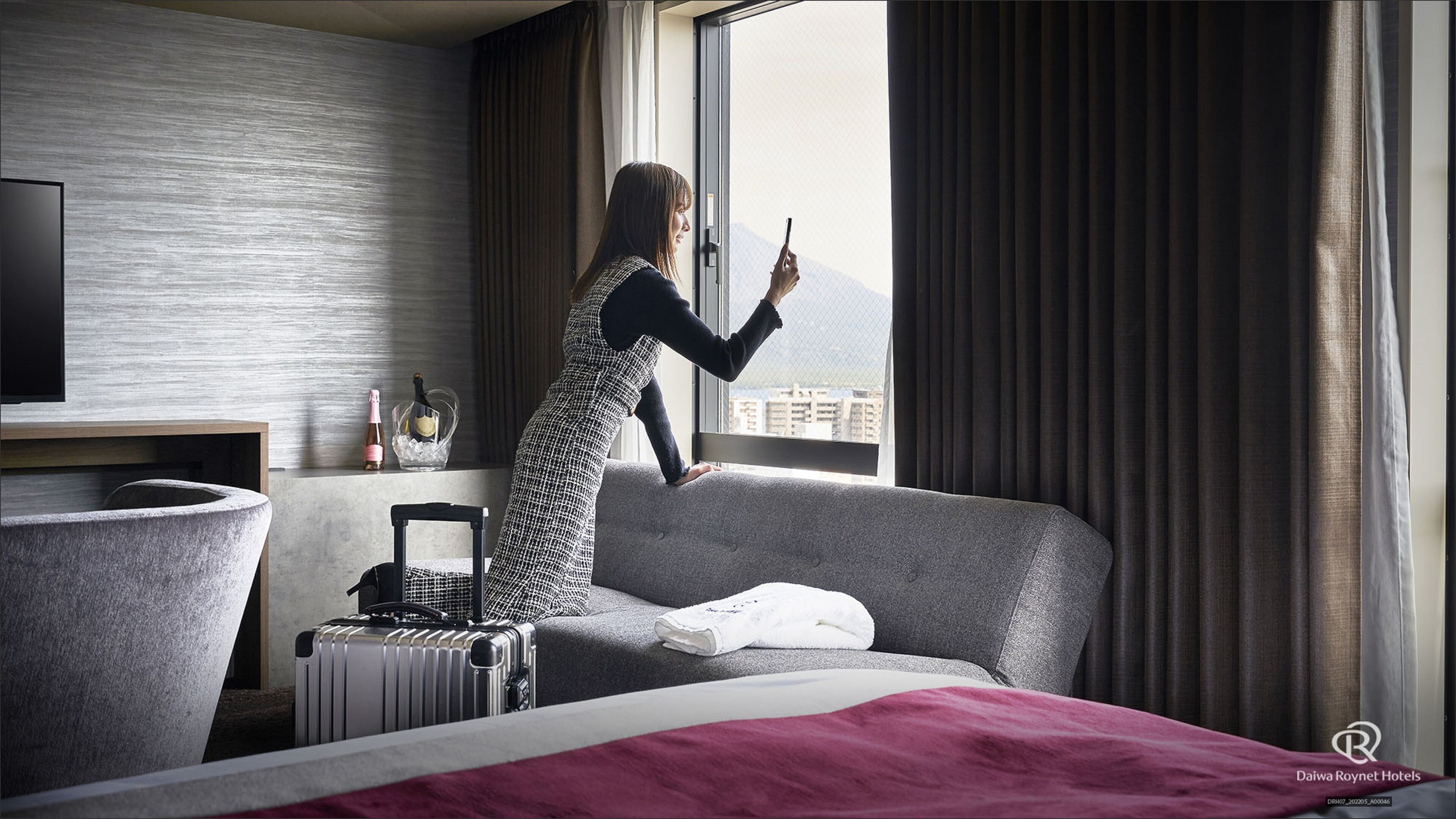 Ett hotellrum med en säng, en resväska, en flaska champagne och utsikt över staden genom fönstret.