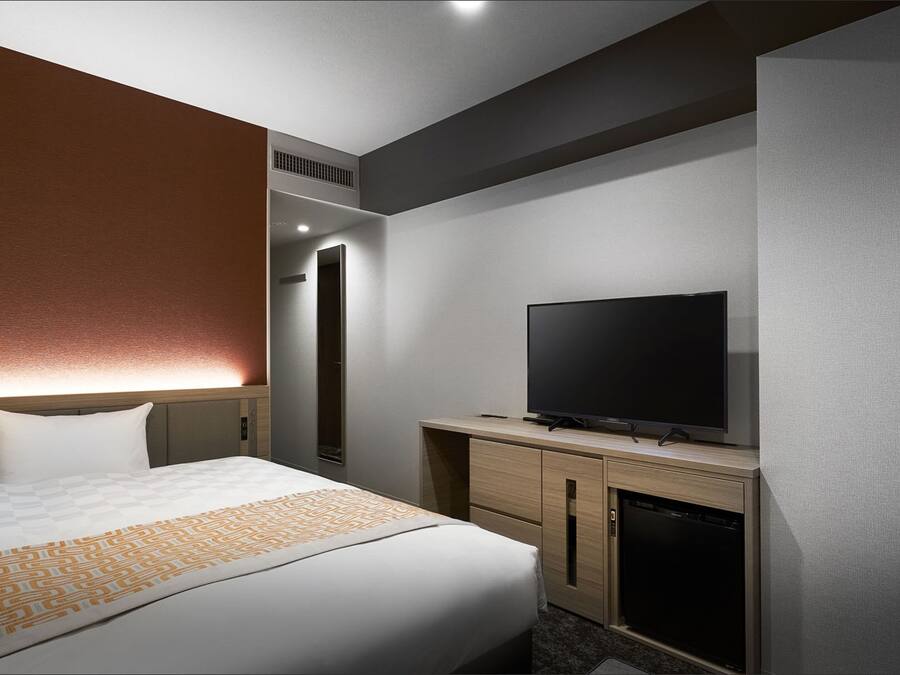 Ein Hotelzimmer mit Bett, Fernseher, Minibar und Spiegel.