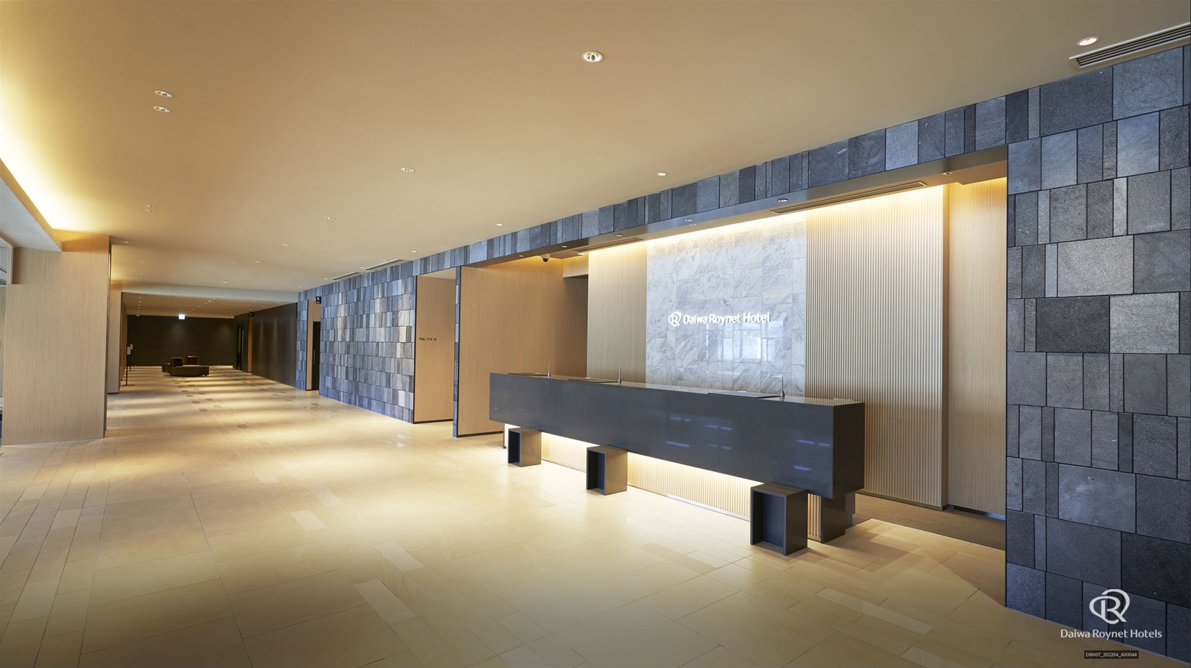 A modern hotel reception area with a long reception desk, a digital display, and a tiled wall.