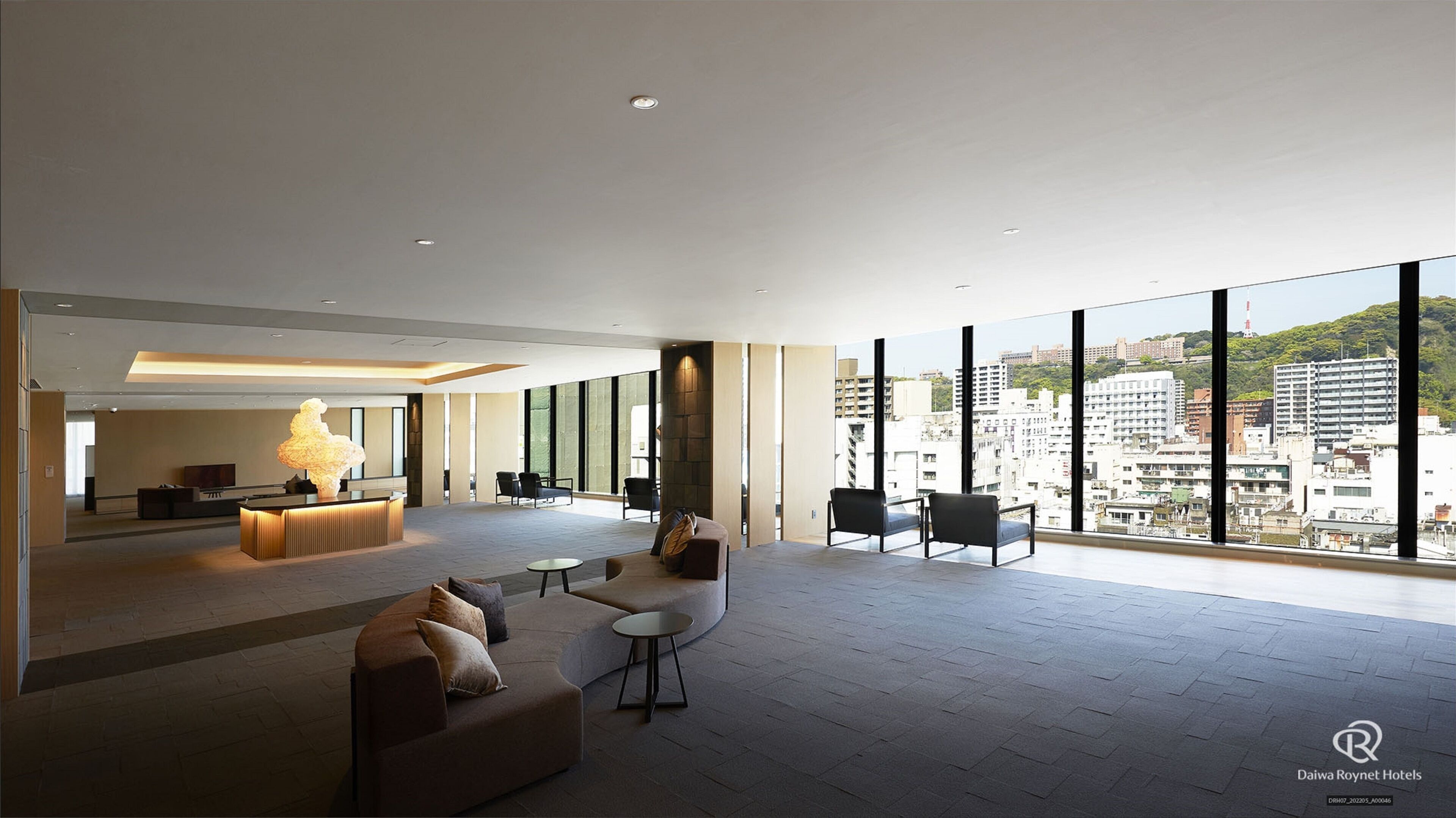 A spacious lobby with a reception desk, seating area, and large windows offering a city view.
