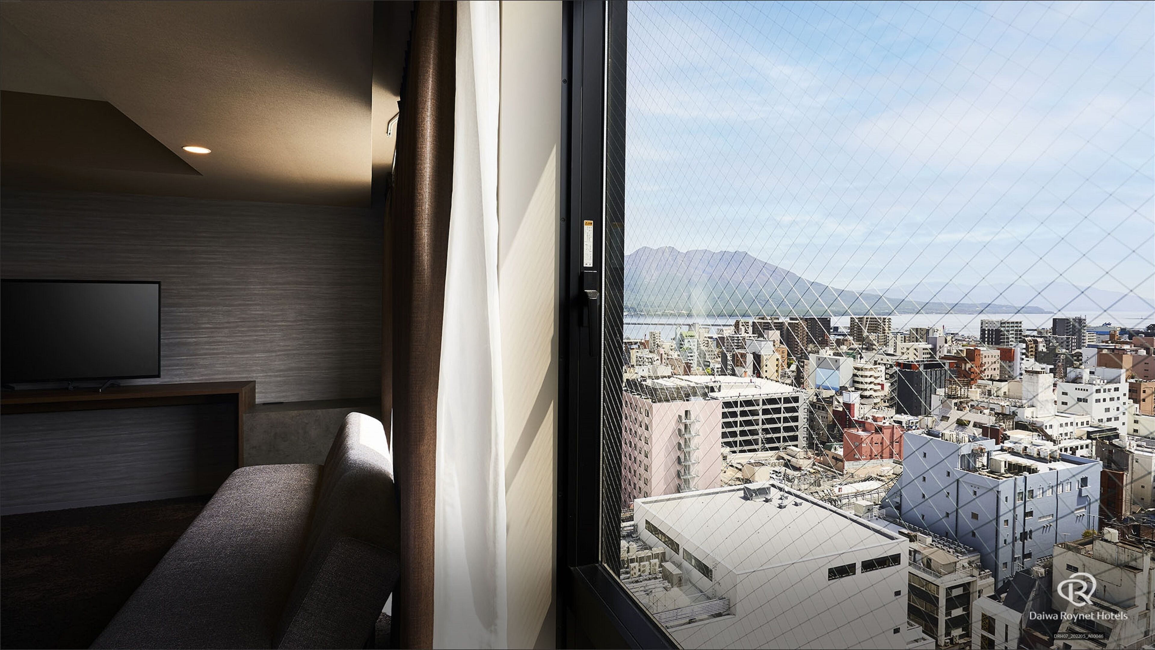 A modern hotel room with a large window offering a cityscape view, a flat-screen TV, and a seating area.