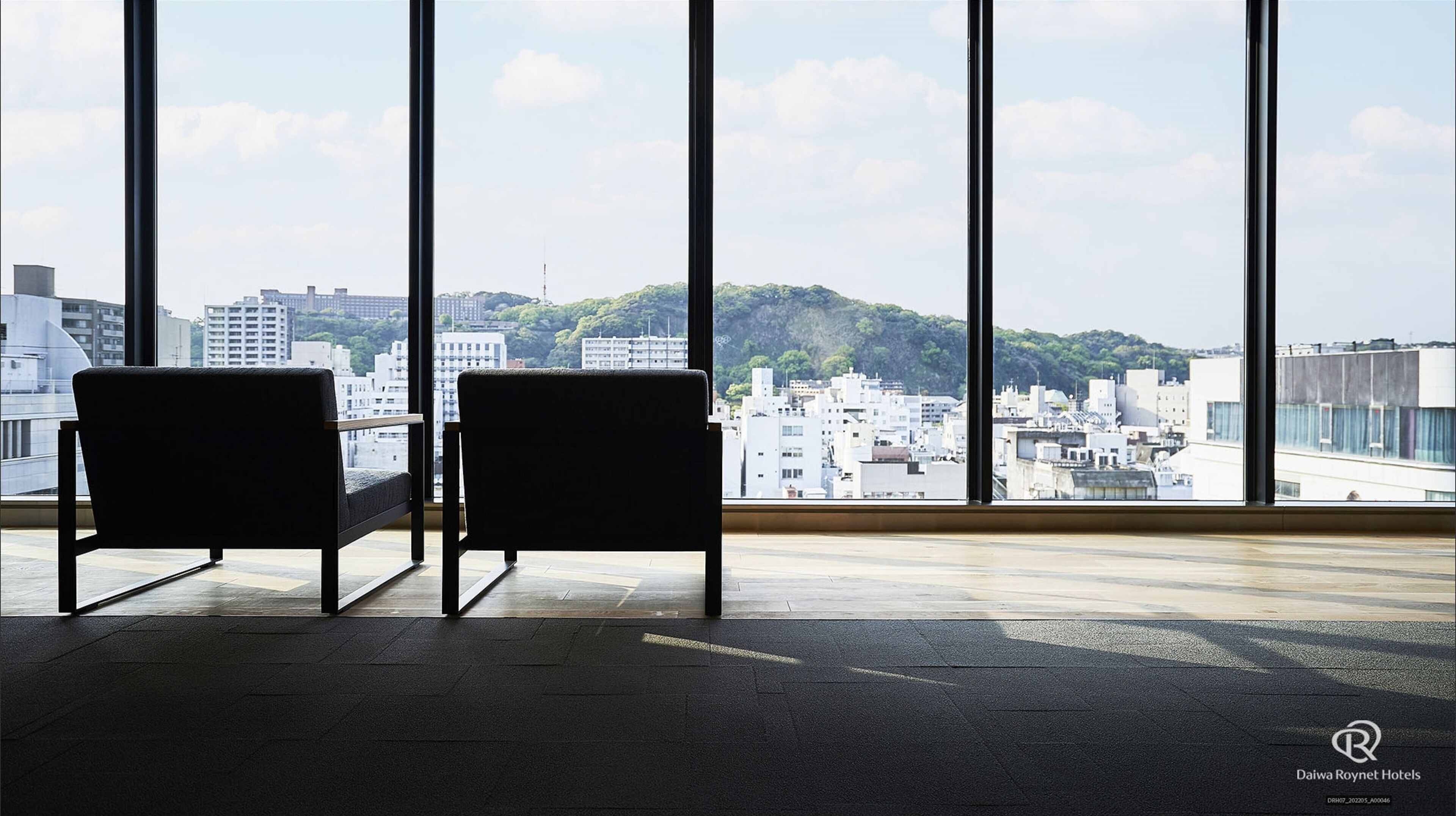 A room with two chairs facing large windows overlooking a cityscape with buildings and greenery.