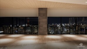 Un interior de hotel moderno con ventanas amplias que ofrecen vista nocturna de la ciudad.