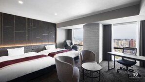 A hotel room with two beds, a desk, a chair, and a large window offering a city view. - Daiwa Roynet Hotel Kagoshima Tenmonkan PREMIER  (Kagoshima)