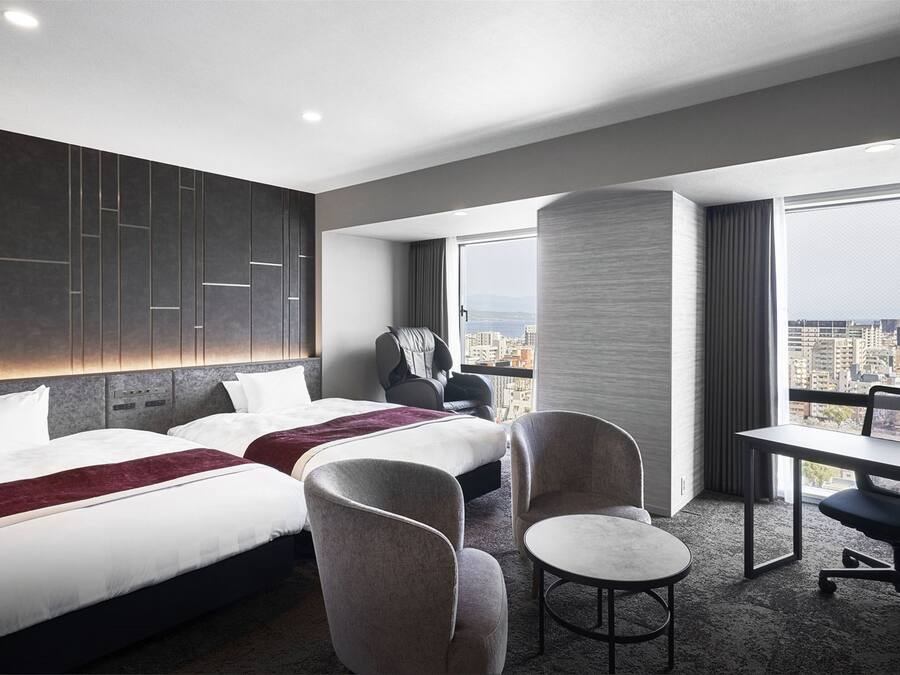 Une chambre d’hôtel avec deux lits, un bureau, une chaise et une grande fenêtre donnant sur la ville.