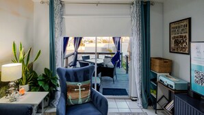 Un soggiorno con una poltrona blu, un tavolino con una lampada e vista su un patio esterno con tavolo e sedie.