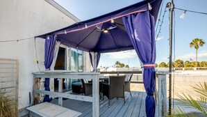 Un'area salotto all'aperto riparata, con un tavolo, sedie, una ventola a soffitto e luci decorative.