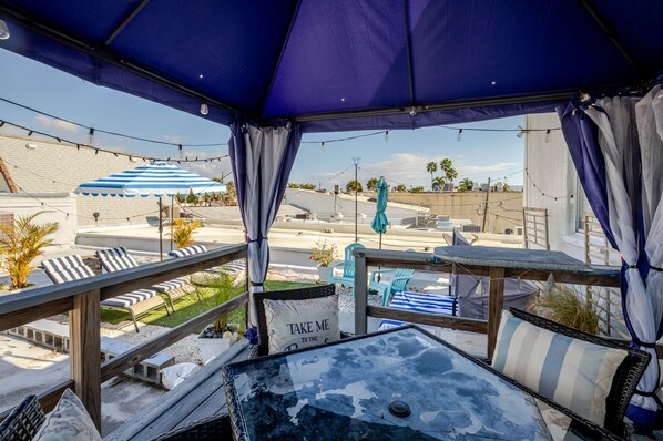 A covered outdoor seating area with striped cushions, a table with a cushion, and a sign that says "TAKE ME TO THE BEACH."