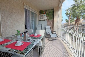 Un balcon avec une table dressée pour deux personnes, des chaises, une cafetière et une plante en pot.