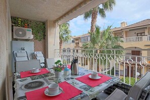 Un balcon avec une table dressée pour deux personnes, un ventilateur de plafond et une vue sur les bâtiments voisins et les palmiers.