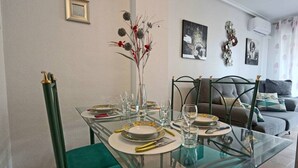 Een eetgedeelte met een glazen tafel gedekt voor vier personen, een vaas met bloemen en een groene stoel.
