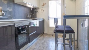 A modern kitchen with dark cabinets, a built-in oven, and a small dining area with a metal table and chairs. - 060 - Gran Playa 004 - comfortHOLIDAYS (Santa Pola)