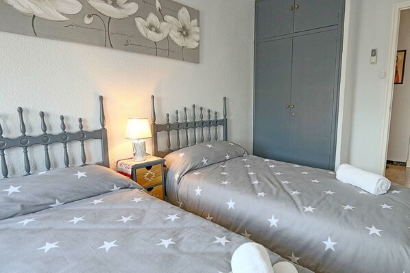 A bedroom with two beds, a nightstand, a lamp, and a wardrobe.