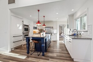 A modern kitchen with white cabinetry, a central island, and red pendant lighting. - Private 1+ acre, Bocce, Waterfall, Free Pool Heat (Santa Rosa)