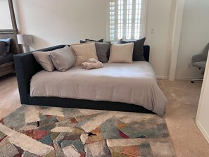 A bedroom with a dark-colored sofa bed, a patterned rug, and a window with blinds. - Private 1+ acre, Bocce, Waterfall, Free Pool Heat (Santa Rosa)