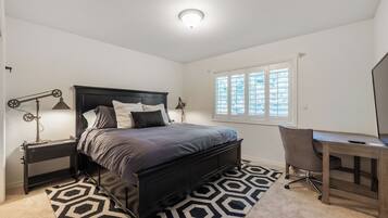 A bedroom with a bed, bedside lamps, a desk, and a window.