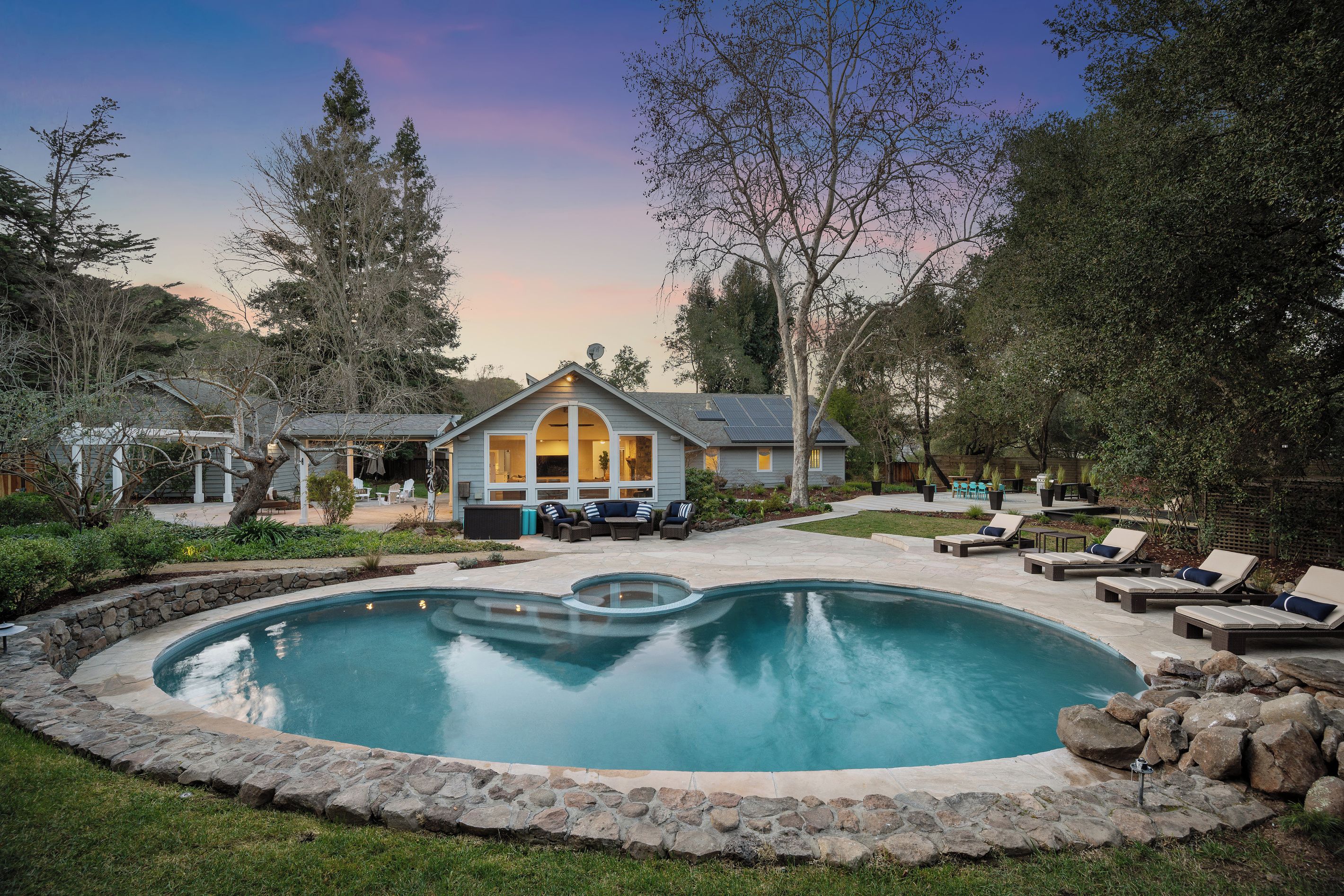 A residential property with a swimming pool, outdoor seating, and a house with a gabled roof.