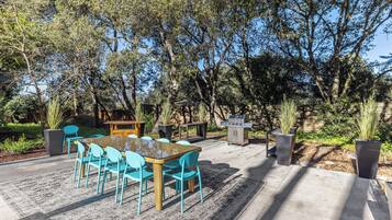 An outdoor patio with a table and chairs, a barbecue grill, and a garden area.
