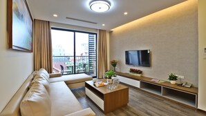 Un salon moderne avec un canapé, une table basse et un téléviseur. Il y a un balcon d’où l’on peut admirer la vue sur les immeubles.