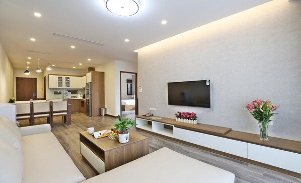 A modern living room with a flat-screen TV, a coffee table with a plant, and a seating area.