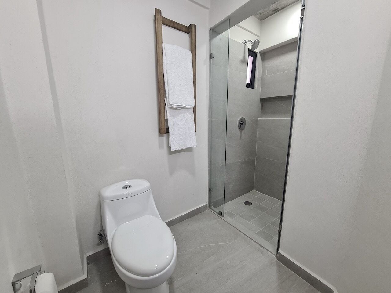 Un baño con inodoro, cabina de ducha de vidrio y toallero de madera.