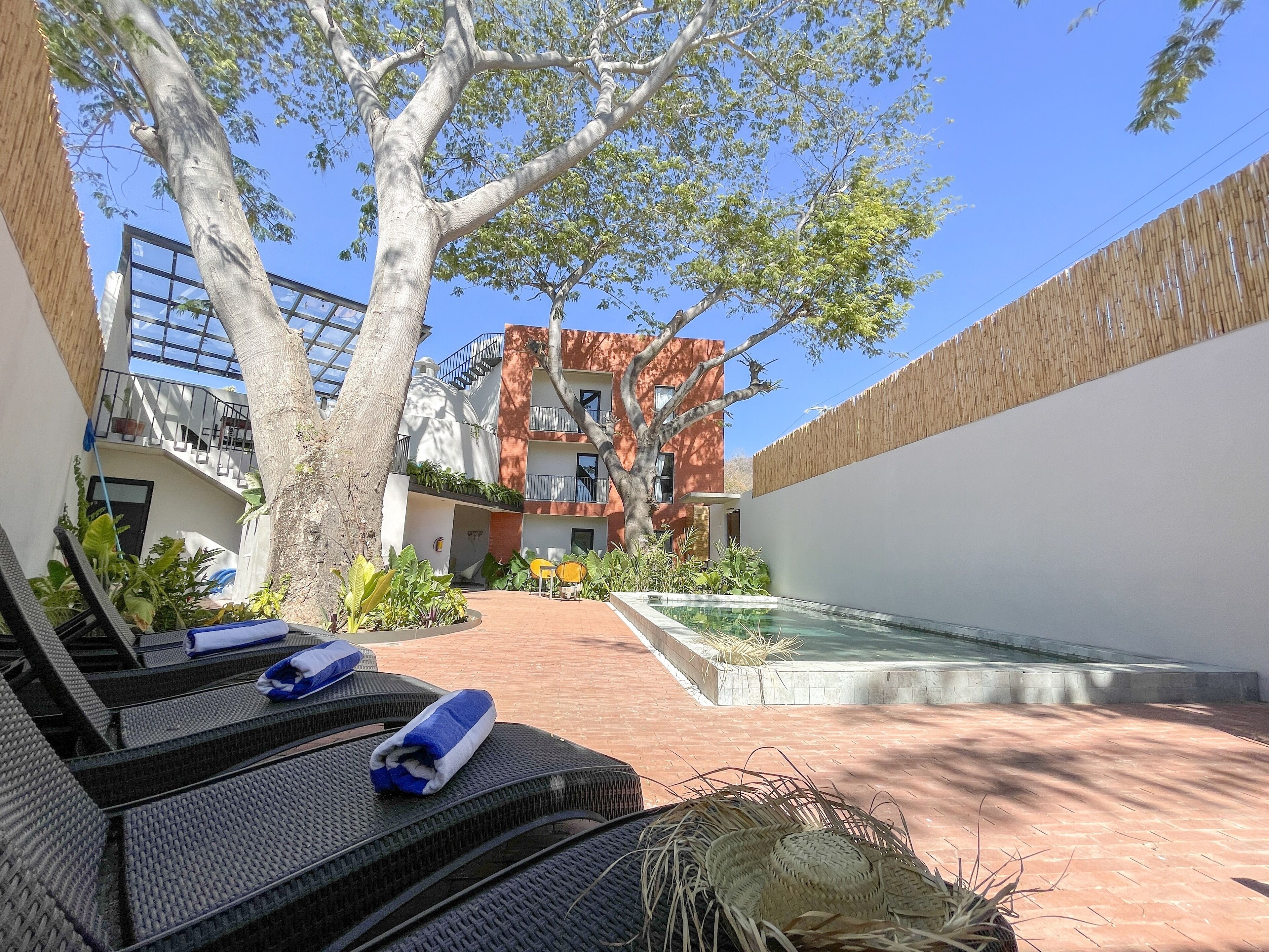 A courtyard with a pool, lounge chairs, and a building with a red facade.