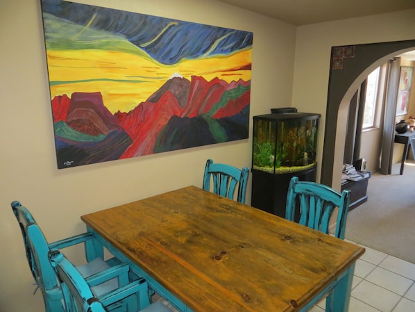 A dining area with a wooden table and turquoise chairs, a colorful painting on the wall, and a fish tank.