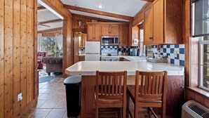 A wooden cabin kitchen with a large island, wooden cabinets, and a checkered backsplash.