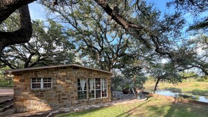 A stone cabin with large windows, a paved patio, and a pond in the background.