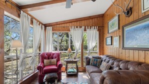 A cozy room with wooden walls, a red armchair, a brown sofa, and a patterned rug.