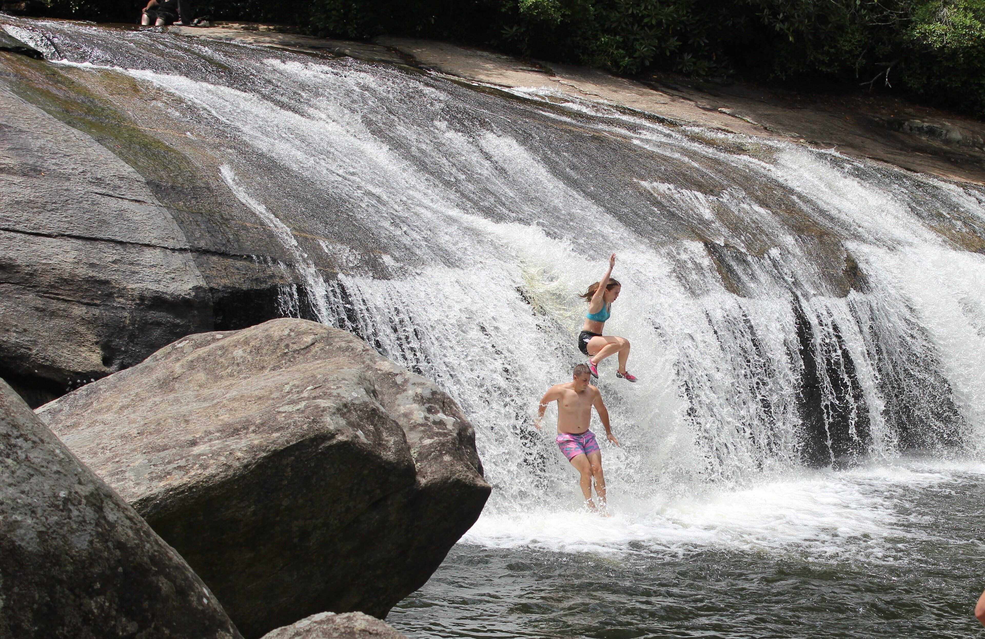 A waterfall with large rocks and a person jumping off.