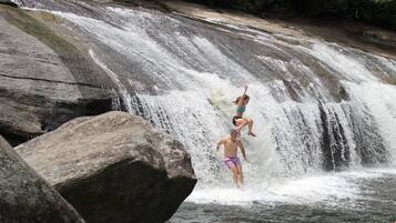 A waterfall with large rocks and a person jumping off.
