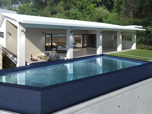 Una casa moderna con piscina, mobiliario exterior y vistas a la vegetación circundante.