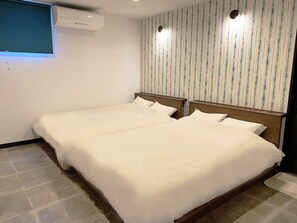 Habitación de hotel con dos camas, una ventana con persianas, un equipo de aire acondicionado y un diseño de papel tapiz a rayas.