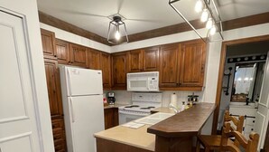 A kitchen with wooden cabinets, a white refrigerator, a microwave, a stove, and a wooden island with a sink. - Best ski-in/ ski-out with A/C and fireplace! (Mont-Tremblant)