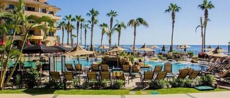 Un complejo turístico con varias piscinas, palmeras y sillas de descanso.