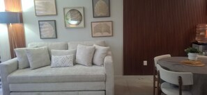 A living room with a sofa, a dining table, and framed artwork on the wall.