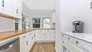 Una cocina moderna con armarios blancos, encimera de madera y una cafetera.