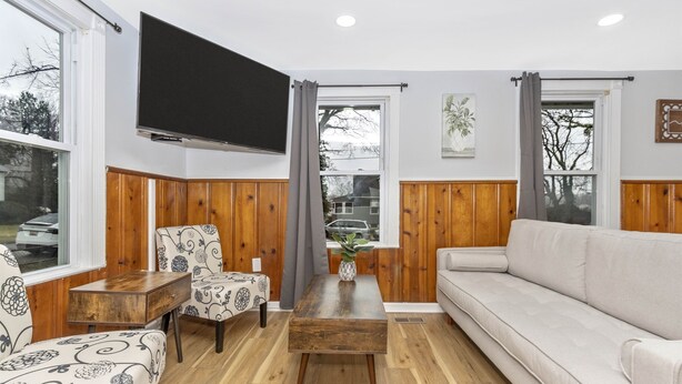 Una sala de estar con un sofá, dos sillones estampados, una mesa de centro de madera y un televisor montado en la pared.