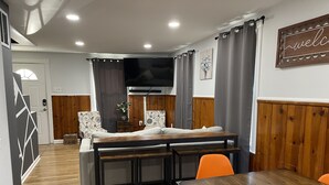 Un comedor con mesa de madera, sillas naranjas, un banco y un televisor montado en la pared.