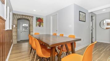 A dining area with a wooden table and orange chairs, a stone archway, and a door with a glass panel.