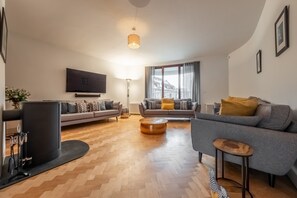 A modern living room with a grey sofa, a round coffee table, and a flat-screen TV mounted on the wall.