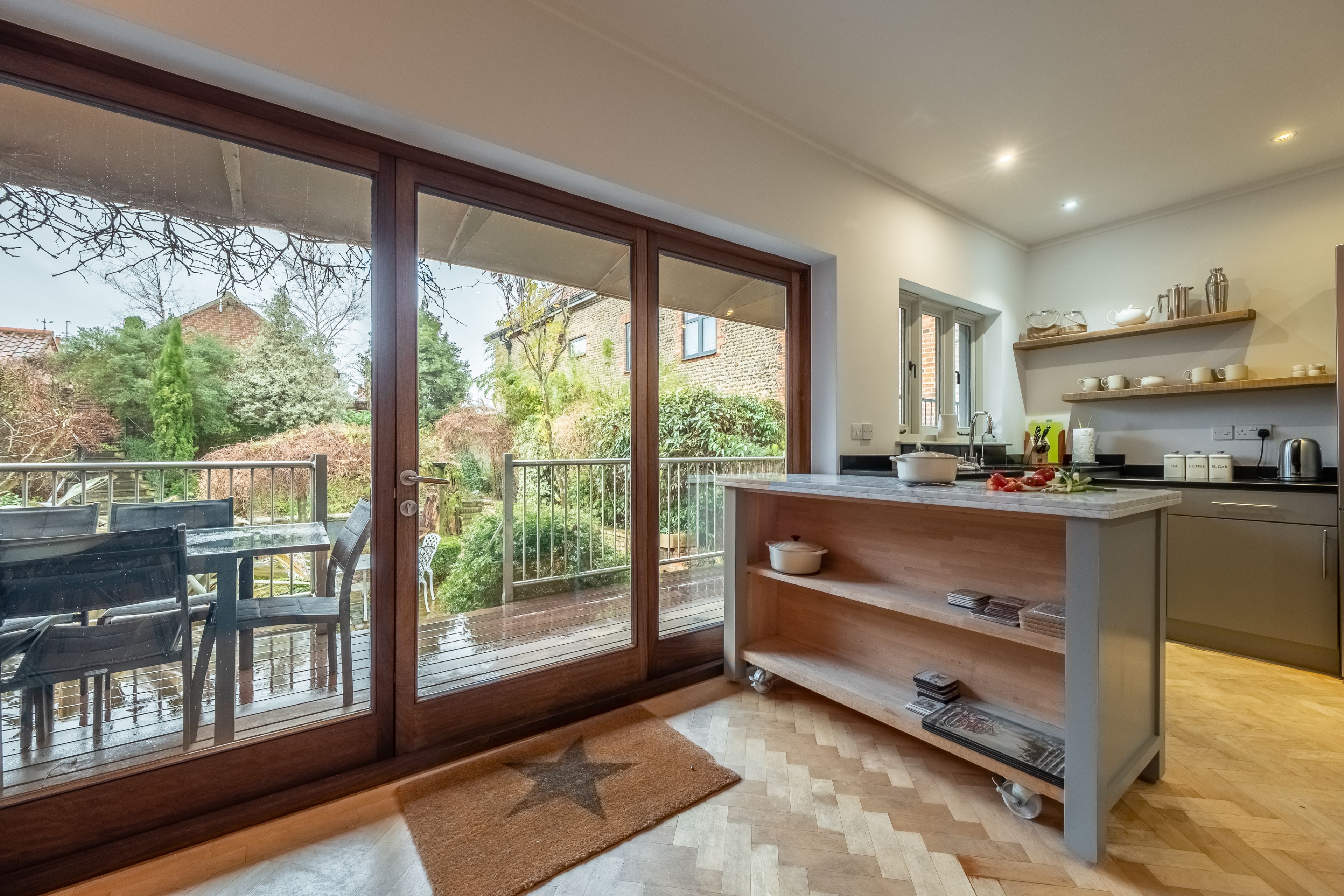 A modern kitchen with a sliding glass door leading to a balcony, a built-in shelf with kitchenware, and a star-patterned rug on the floor.