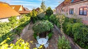 A courtyard with a brick pathway, white outdoor furniture, and lush greenery. - The Roundhouse, Wells-next-the-Sea, Norfolk (Wells-next-the-Sea)