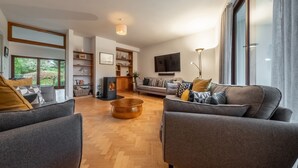 A modern living room with a fireplace, grey sofas, and a large window. - The Roundhouse, Wells-next-the-Sea, Norfolk (Wells-next-the-Sea)