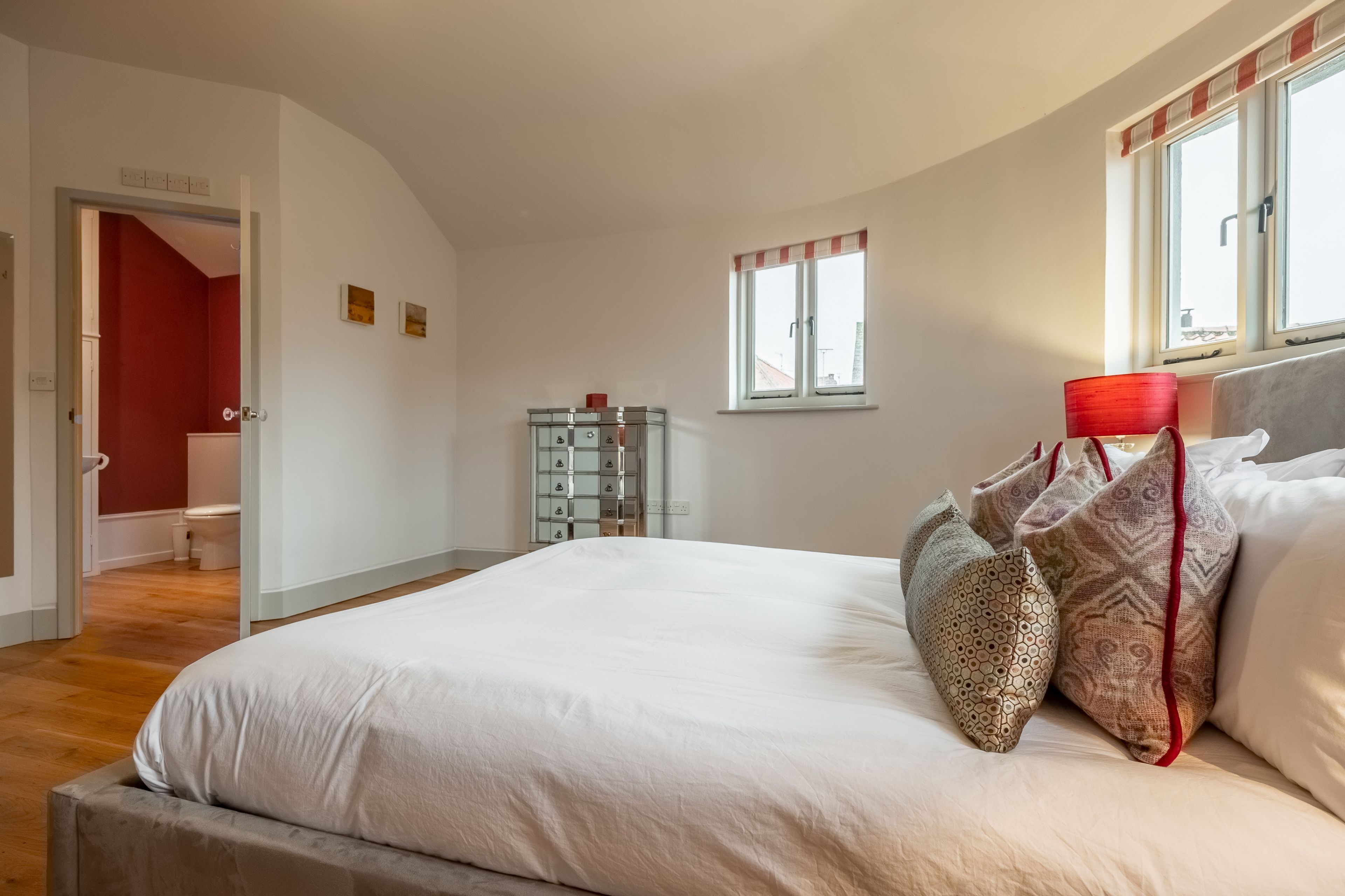 Een slaapkamer met een groot bed, een rode lamp en een raam met gordijnen.